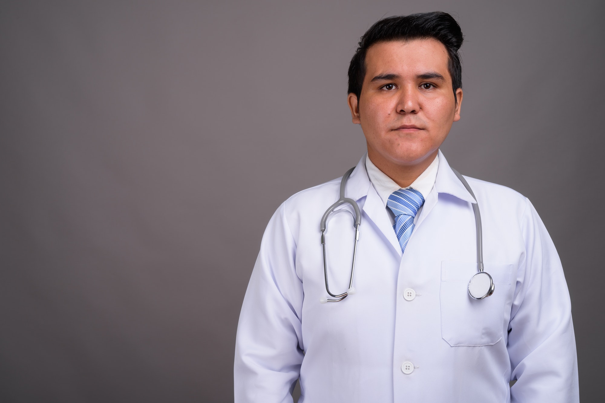 Young multi-ethnic man doctor against gray background