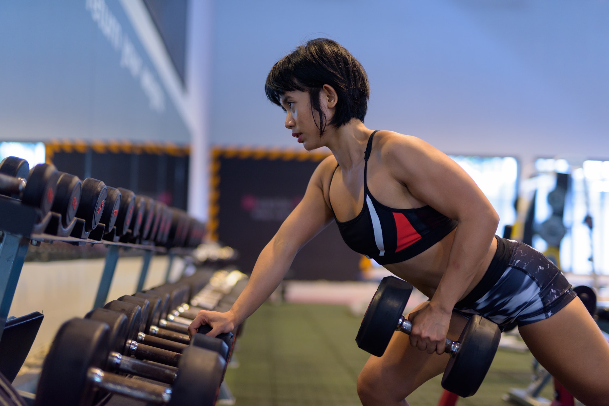 Young beautiful Asian woman doing dumbbell row in gym