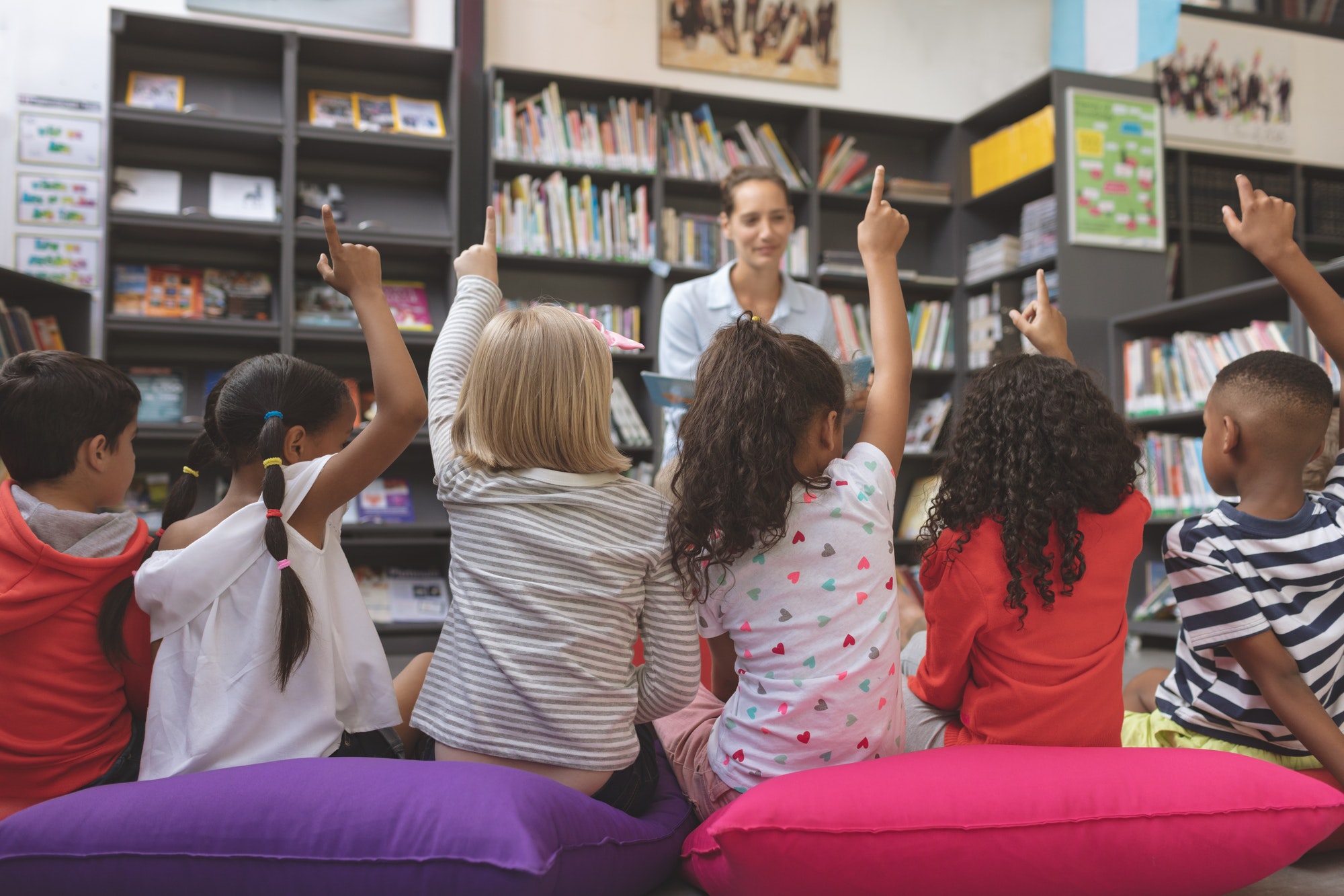 Schoolkids raising hand to answer at a question asking agaisnt bookshelf