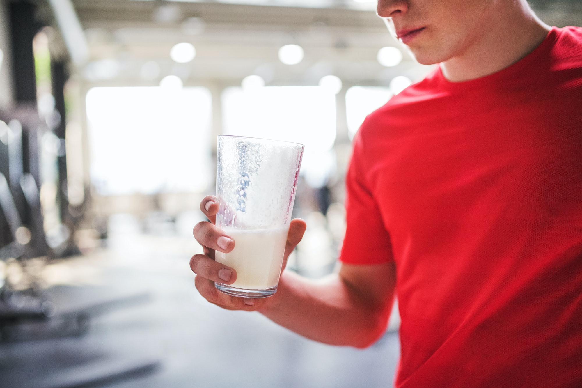 Young man in gym holding a glass of protein drink. Copy space.