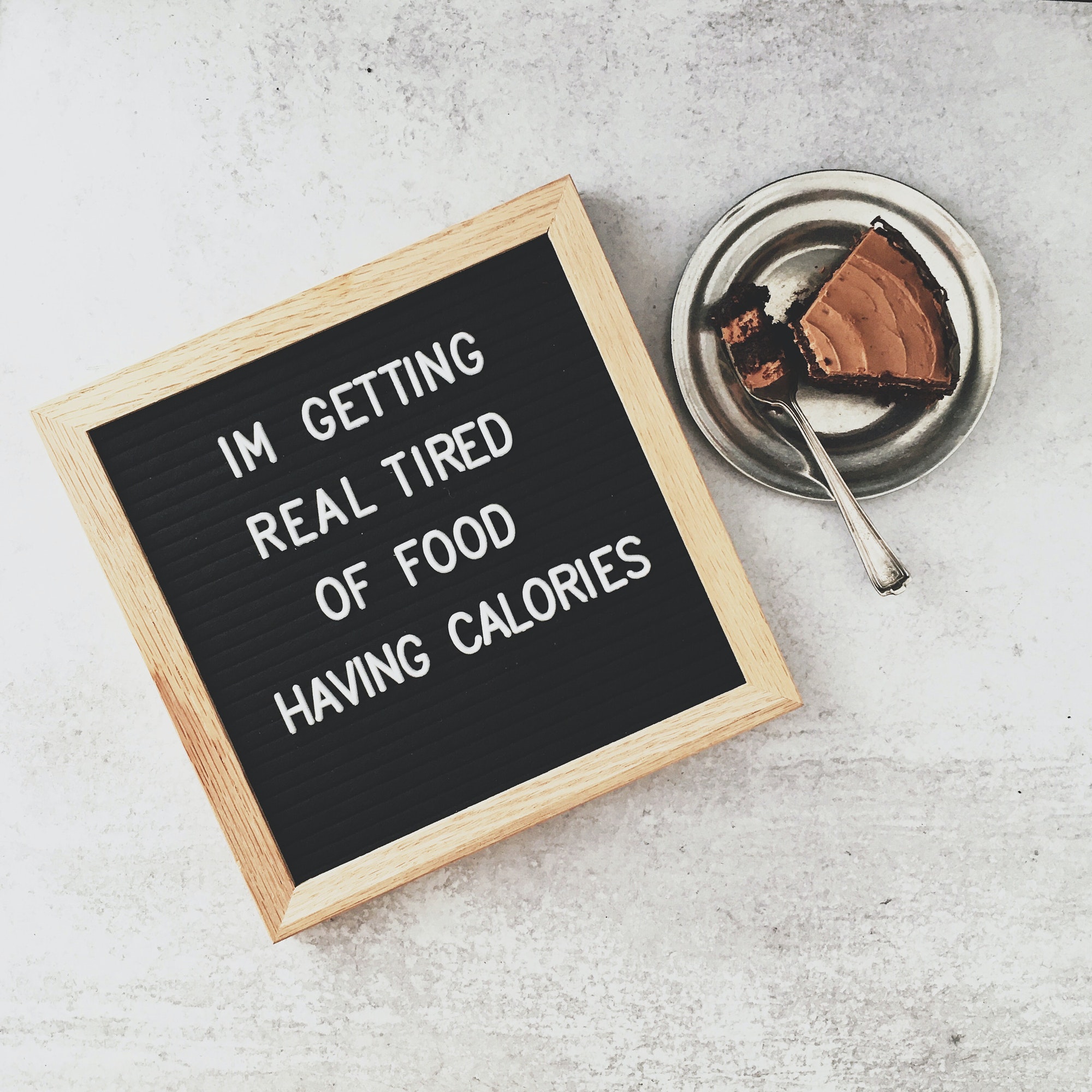 Humorous Letter board about calories, sitting next to a slice of chocolate cake, grey background