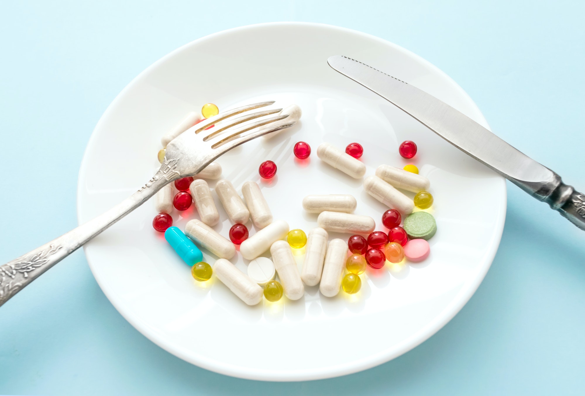Many different weight loss pills and supplements as food on round white plate with fork and knife Many different weight loss pills and supplements as food on round white plate with fork and knife